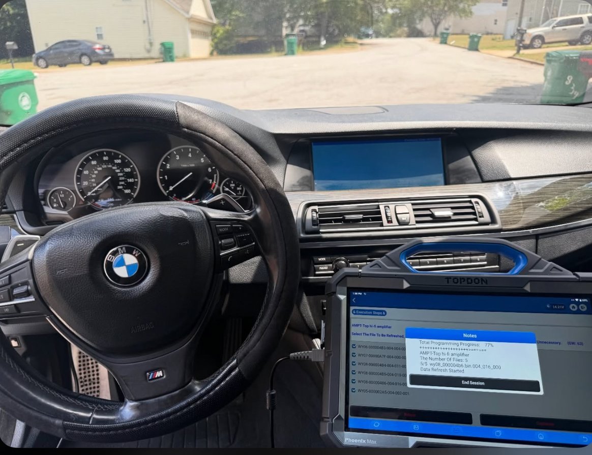 BMW car interior dashboard with steering wheel and diagnostic laptop screen showing vehicle data