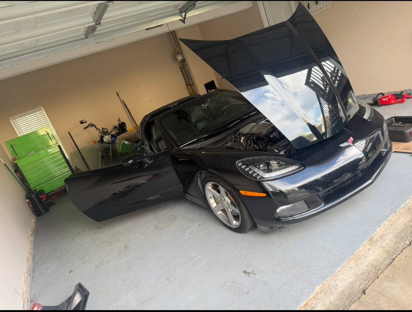 Black sports car with open hood in garage, showing engine compartment during maintenance
