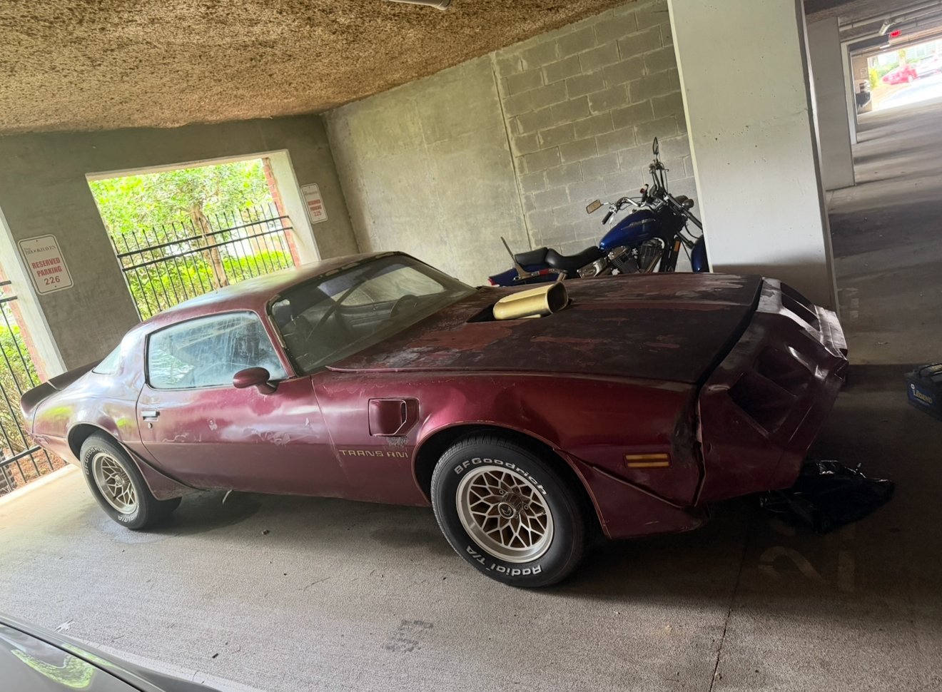 Maroon vintage sports car parked in a garage with a motorcycle and equipment on its roof