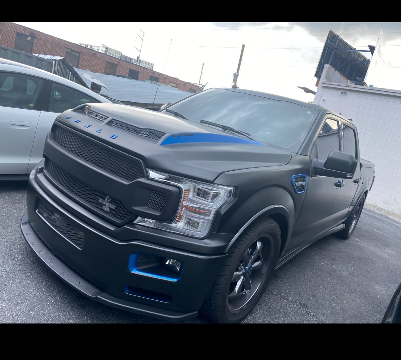 Black Ford F-150 truck with blue accents parked at a dealership lot with other vehicles in the background